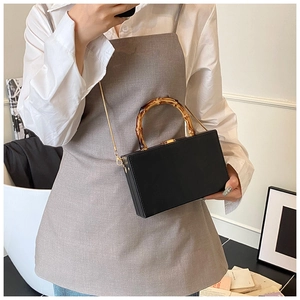 Close-up of minimalist black box bag with authentic bamboo handle and gold chain strap