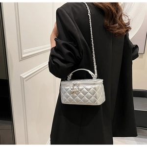 Detail view of silver quilted box bag with heart pendant and metallic chain strap