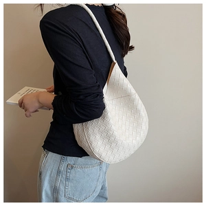 Gros plan d'un grand sac cabas blanc en cuir tressé porté à l'épaule par le modèle