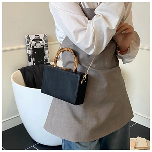 Detail of black box handbag with bamboo handle and gold chain strap on stylish outfit