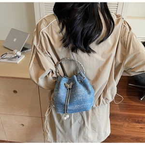 Back view of a blue denim bucket bag with silver chain strap and pearl butterfly charm