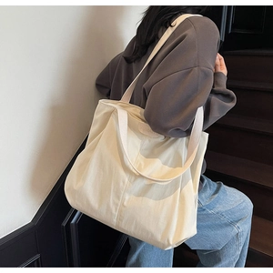 Detail of the cream-white canvas tote bag featuring JUMAN leather label and wide straps