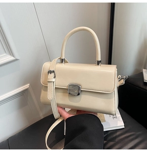 Close-up of cream square handbag showing smooth leather texture and silver lock detail