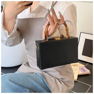 Detail view of black leather box handbag featuring vintage bamboo handle and gold lock