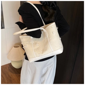 Close-up of a cream tote bag with 3D floral textures and premium white leather straps