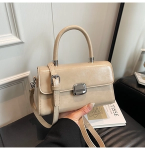 Detail of cream faux leather handbag featuring a square silver buckle and top handle
