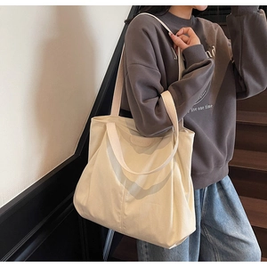 Detailed shot of large cream canvas tote bag with leather logo patch worn by model