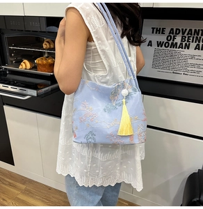 Detail of light blue bucket bag with intricate floral embroidery and yellow tassel