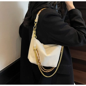 Detail of a creamy nylon dumpling bag with golden chain and woven strap on black blazer
