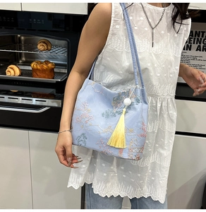 Close-up of light blue embroidery bucket bag with elegant floral pattern and yellow tassel