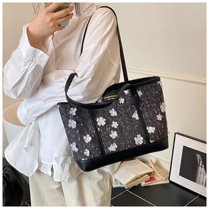 Close-up of black tweed tote bag featuring white 3D floral appliqués and metal logo