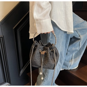 Close-up of denim bucket bag with sparkling rhinestones, butterfly charm, and pearl tassel