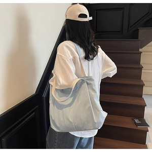 Detail of light blue canvas tote bag showing large capacity worn by a model in a minimal setting