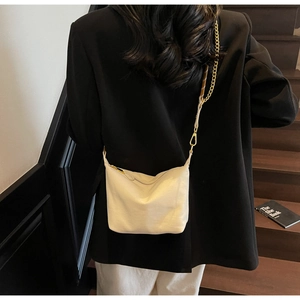 Detail of cream nylon crossbody bag with gold chain strap on model in urban setting