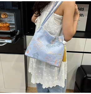 Detail of light blue embroidered bucket bag with pearl strap and yellow tassel pendant
