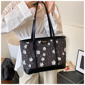 Detail of black tweed tote bag with 3D white flowers and golden metal logo plate