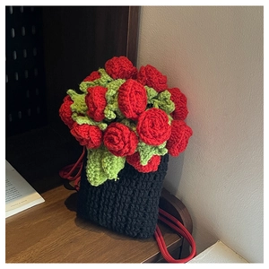 Detail of a handmade crochet bucket bag featuring red roses and green leaves on black yarn