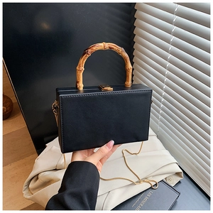 Close-up of black matte square bag with natural bamboo handle and golden clasp