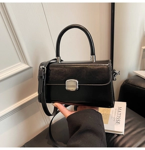 Detail of vintage black leather handbag with silver lock being held by a model