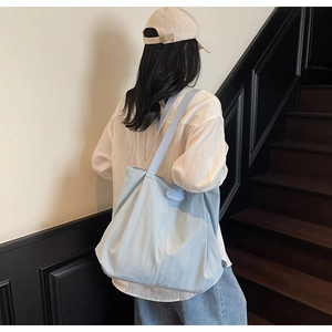 Light blue canvas tote bag side view with leather brand tag in a casual urban setting
