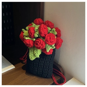 Detail of handcrafted crochet bucket bag with red roses and green leaves on wooden table