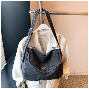 Dettaglio borsa a tracolla in denim scuro con chiusura a scatto in metallo e tracolla regolabile