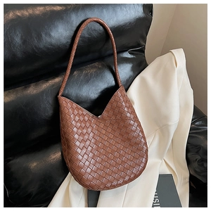 Gros plan sur un sac hobo en cuir tressé marron posé sur un canapé en cuir noir
