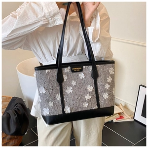 Close-up of grey tweed tote bag featuring white 3D floral accents and gold brand nameplate