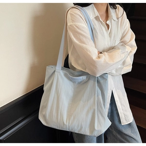 Close-up of light blue large capacity tote bag with logo detail on a wooden staircase
