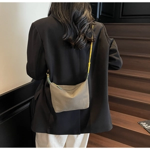 Detail of grey nylon crossbody bag with yellow strap worn over a black blazer