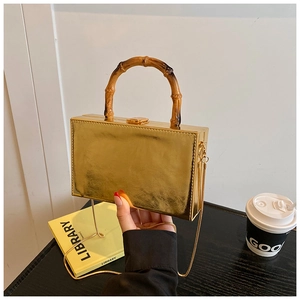 Detail of a vintage golden hardshell mini bag featuring a chic bamboo top handle