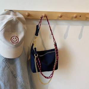 Detail of black nylon crossbody bag with red braided rope strap and gold metal chain