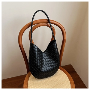 Détail du sac hobo en cuir tressé noir présentant une texture intrecciato sur une chaise en bois
