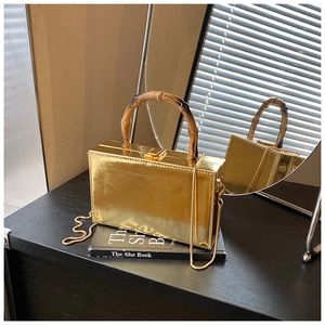 Detail view of gold mirror finish handbag with natural bamboo handle and gold chain strap