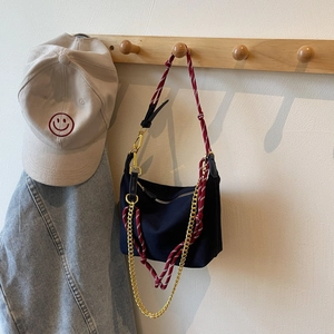 Detail of black nylon bag with red and white woven strap and gold chain on wooden rack