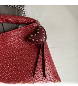 Detail of red woven bucket bag featuring heart rivet charm and metal chain strap