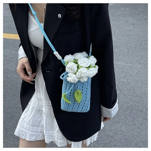 Détail d'un sac seau au crochet bleu ciel avec des fleurs de roses blanches porté par un mannequin