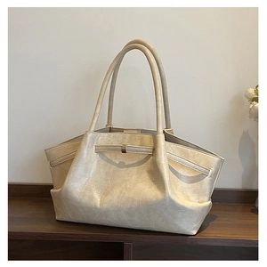 Detailopname van de crèmekleurige tote bag met krokodillenprint en goudkleurige gesp op hout