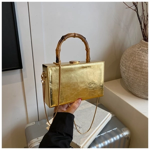 Detail of a gold rectangular box bag featuring a bamboo top handle and chain strap