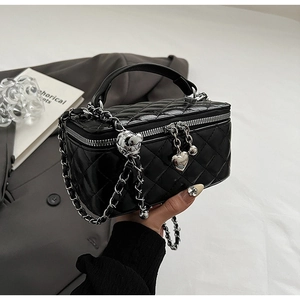 Detail of black quilted leather handbag with gold chain strap and heart pendant