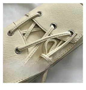 Detail of cream faux leather shoulder bag featuring silver eyelets and cross-tie bow design