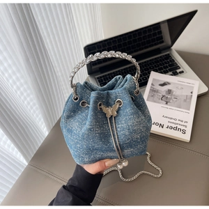 Detail of light blue denim bucket bag with rhinestone handle and metal butterfly charm