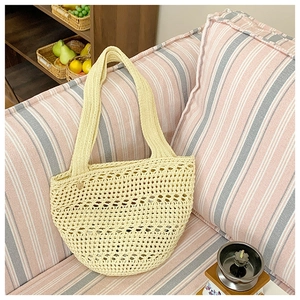 Close-up of a hollow knit tote bag with a beige crochet pattern on a striped sofa