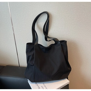 Close-up of black canvas tote bag with leather logo patch on a white art book