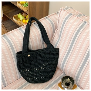 Detail of black hollow-out crochet tote bag with golden metal tag on a soft striped sofa