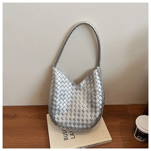 Gros plan d'un sac hobo tissé argenté montrant la texture métallique sur des livres