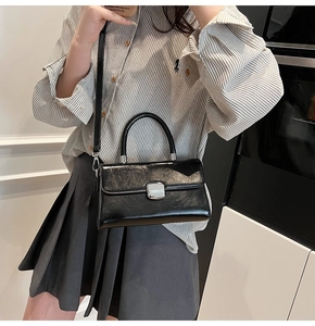Detail of black patent leather handbag featuring silver rectangular metal lock and top handle