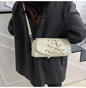 Detail of cream white pleated patent leather bag with lace-up eyelets on gray blazer
