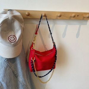 Detail view of red nylon crossbody bag with braided rope strap and gold metal chain