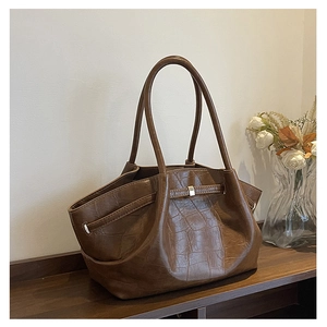Detail van een donkerbruine shopper met krokodillenmotief en een metalen vierkante gesp
